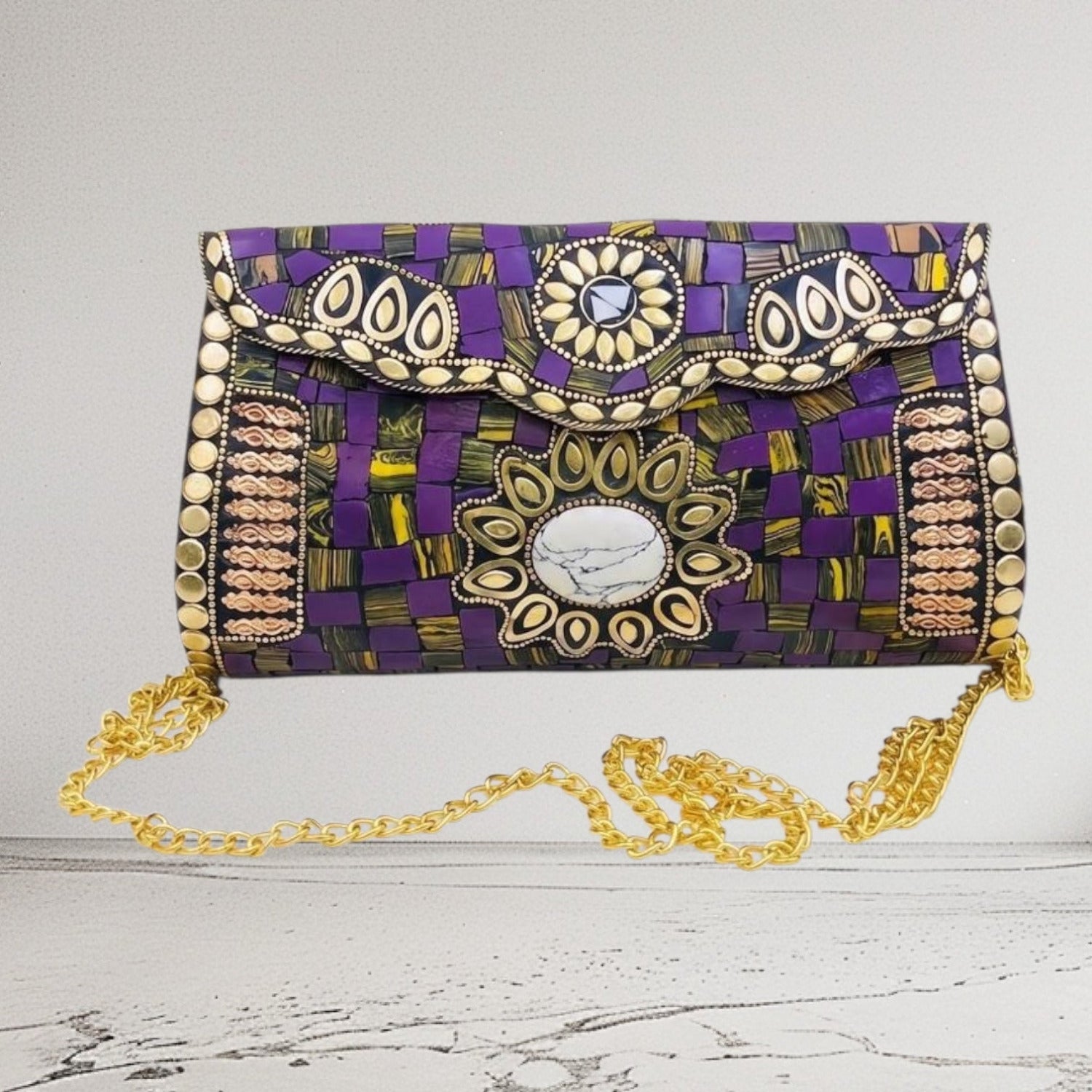 A purple woven clutch bag with gold and silver metallic embellishments, a central oval mirror, and a gold chain strap, displayed on a light gray background.