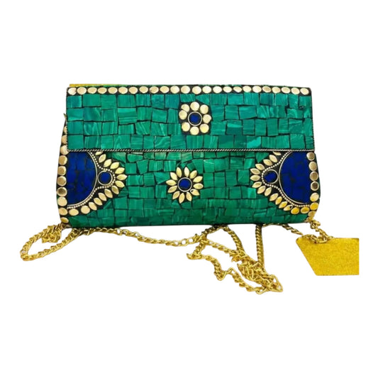 A woven clutch bag in green and blue raffia with gold metallic embellishments, a gold chain strap, and a yellow tag, shown against a light gray background.