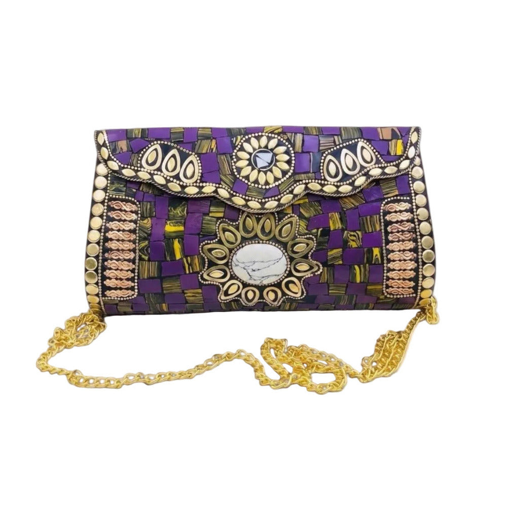 A purple and black patterned clutch bag with gold and silver metallic embellishments, featuring a scalloped flap, a central oval medallion, and a gold chain strap, set against a light gray background.