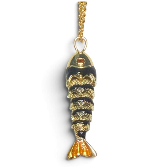 A small fish-shaped pendant charm with a gold-tone chain, featuring black and gold enamel detailing with a small red accent near the head, set against a plain white background.